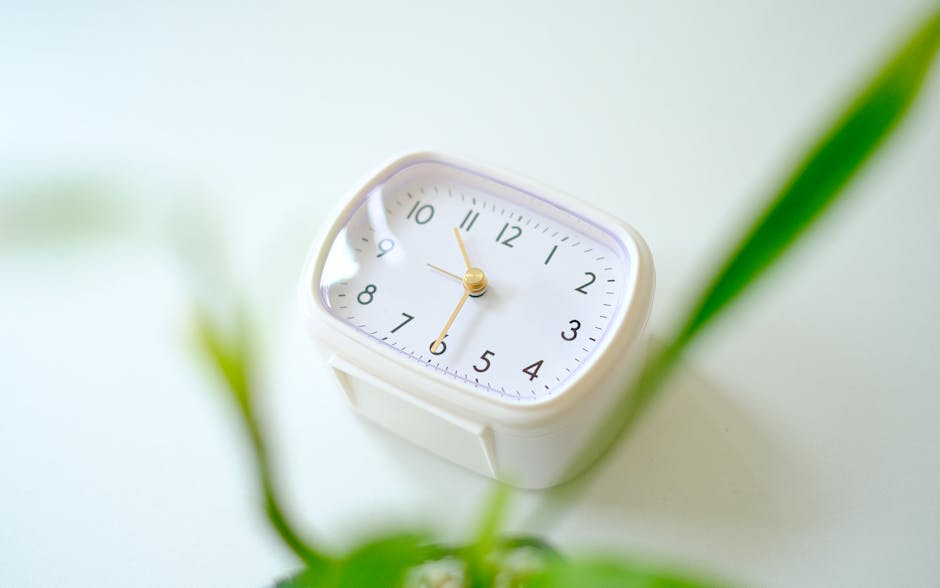 A minimalist white clock on a desk with blurred green leaves, creating a serene workspace vibe.
