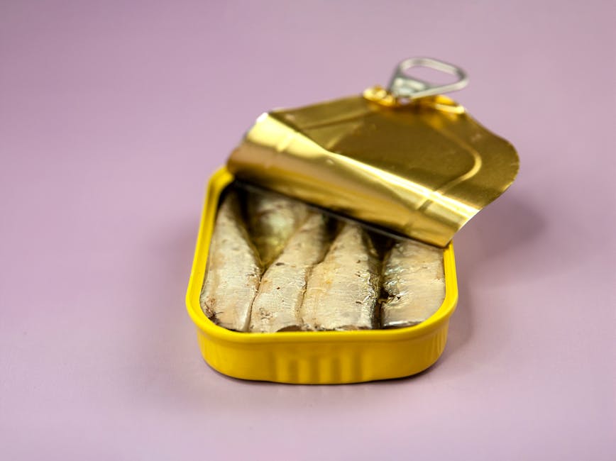 Close-up of an open sardine tin, showcasing fresh fish fillets on a purple backdrop.