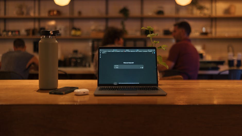 Laptop in a cozy café setting with people in the background, warm lighting.