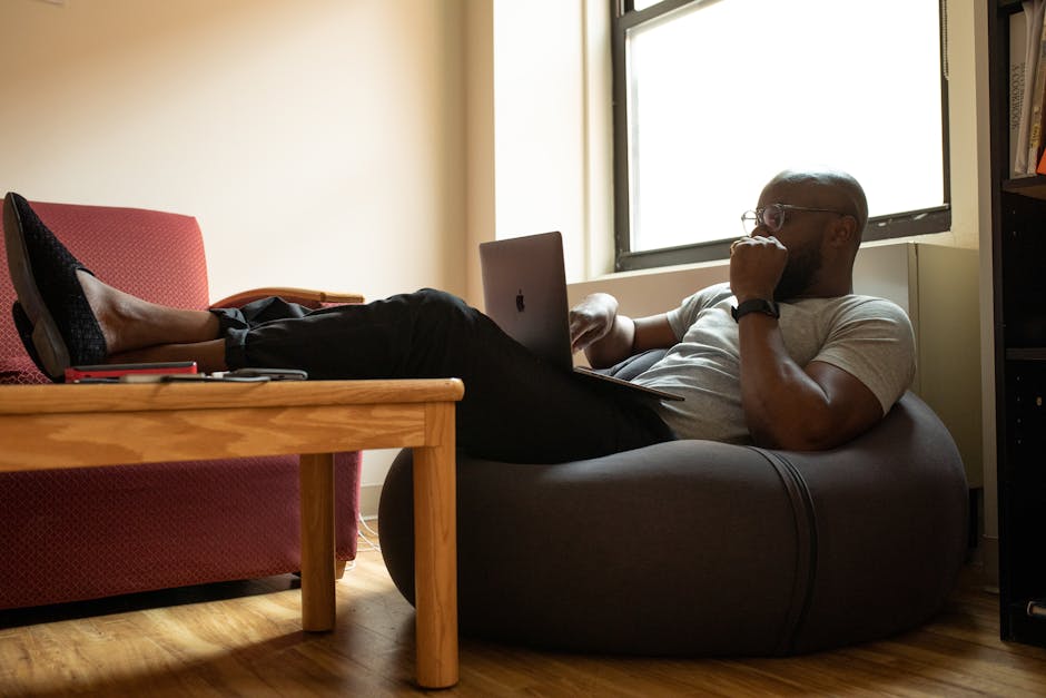 A man working remotely on a laptop while reclining comfortably in a modern home office.