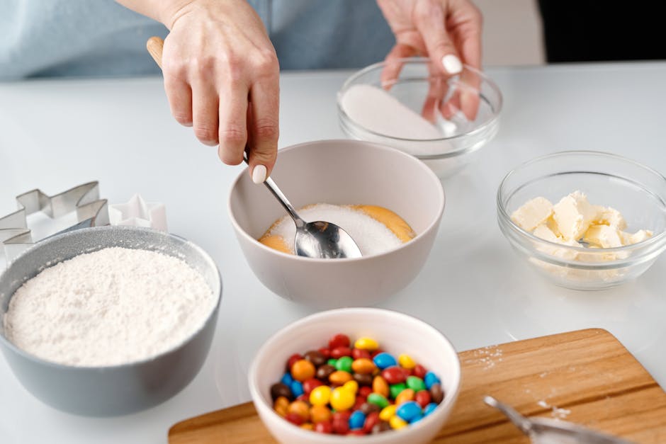 Hands mixing ingredients for baking, including flour, sugar, butter, and chocolate candies.