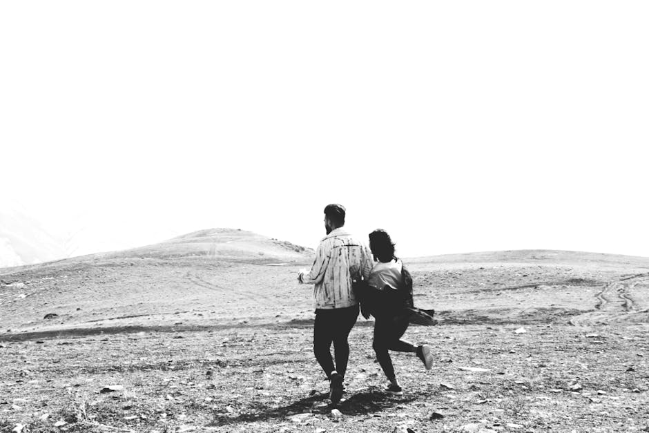 A couple joyfully runs through a vast desert landscape captured in black and white.