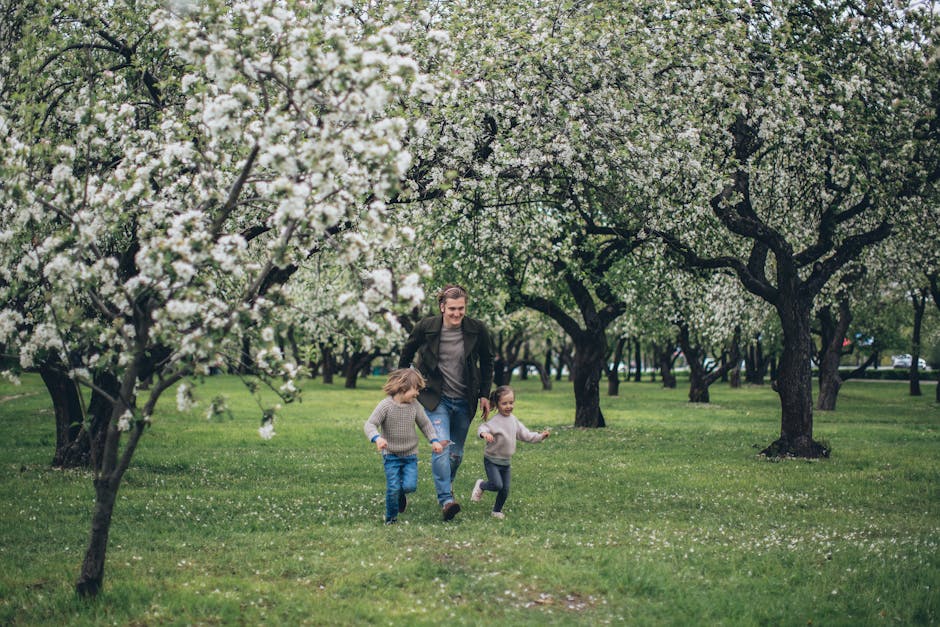 Father and children running joyfully in a lush, blossoming spring orchard.